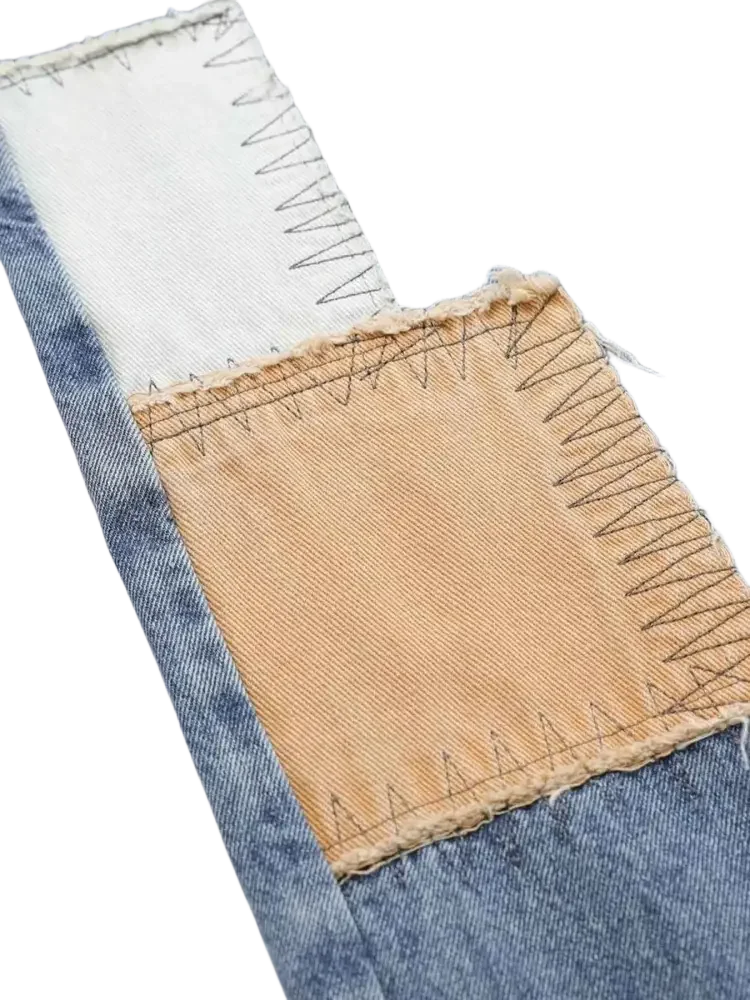 Close-up of vintage patchwork wide leg jeans with white and tan patches and black zigzag embroidery
