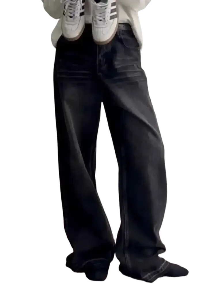 Person wearing loose-fitting faded black wide leg jeans holding white sneakers with black stripes