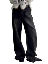 Person wearing loose-fitting faded black wide leg jeans holding white sneakers with black stripes